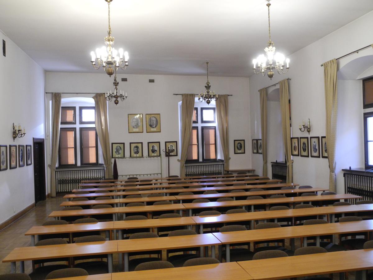 Wnętrze sali wykładowej nr 39, na pierwszym planie stoły, w głębi na ścianach rozwieszone portrety profesorów